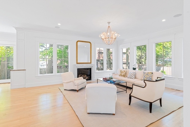 Bright living room with fireplace, high ceilings, and large windows framing the green tree canopy